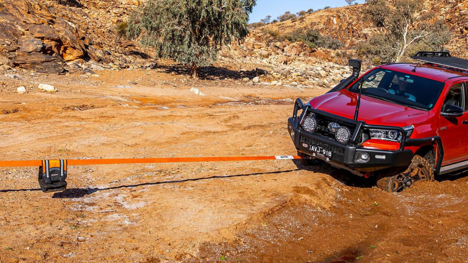 A stuck 4x4 truck connected by an orange ARB snatch strap to the ARB Recovery bag on the trail