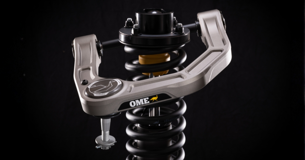 Old Man Emu Forged Billet upper control arm mounted on a coil spring and shock, shown on a black background