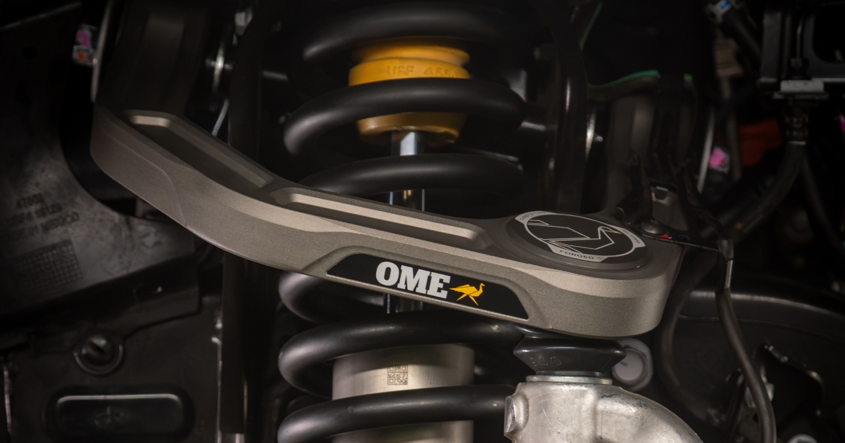 Close-up of the gray Old Man Emu Forged Billet upper control arm installed above the coil spring in a truck’s front suspension
